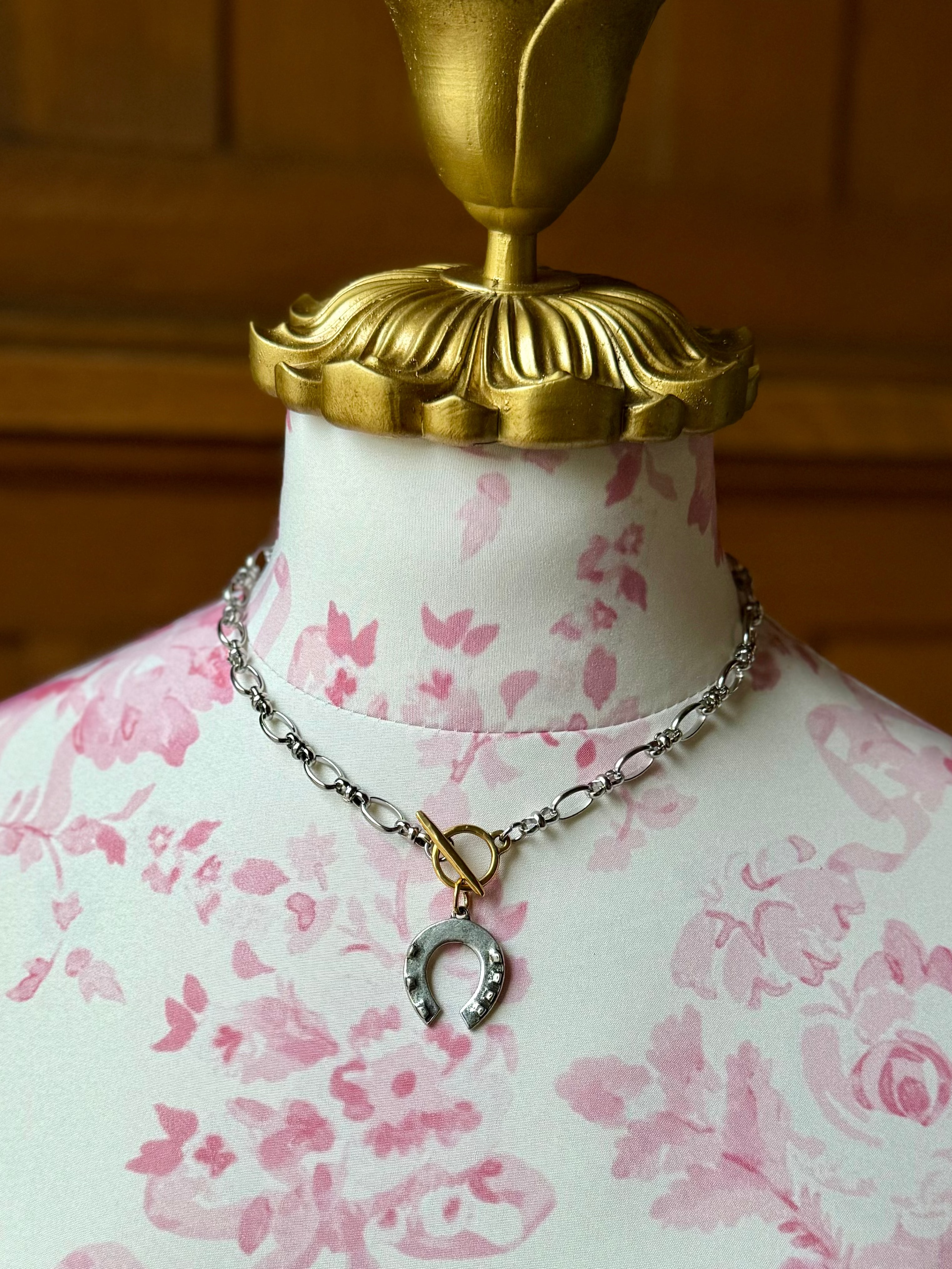 Mannequin torso with pink floral pattern wearing a necklace with a horseshoe pendant.
