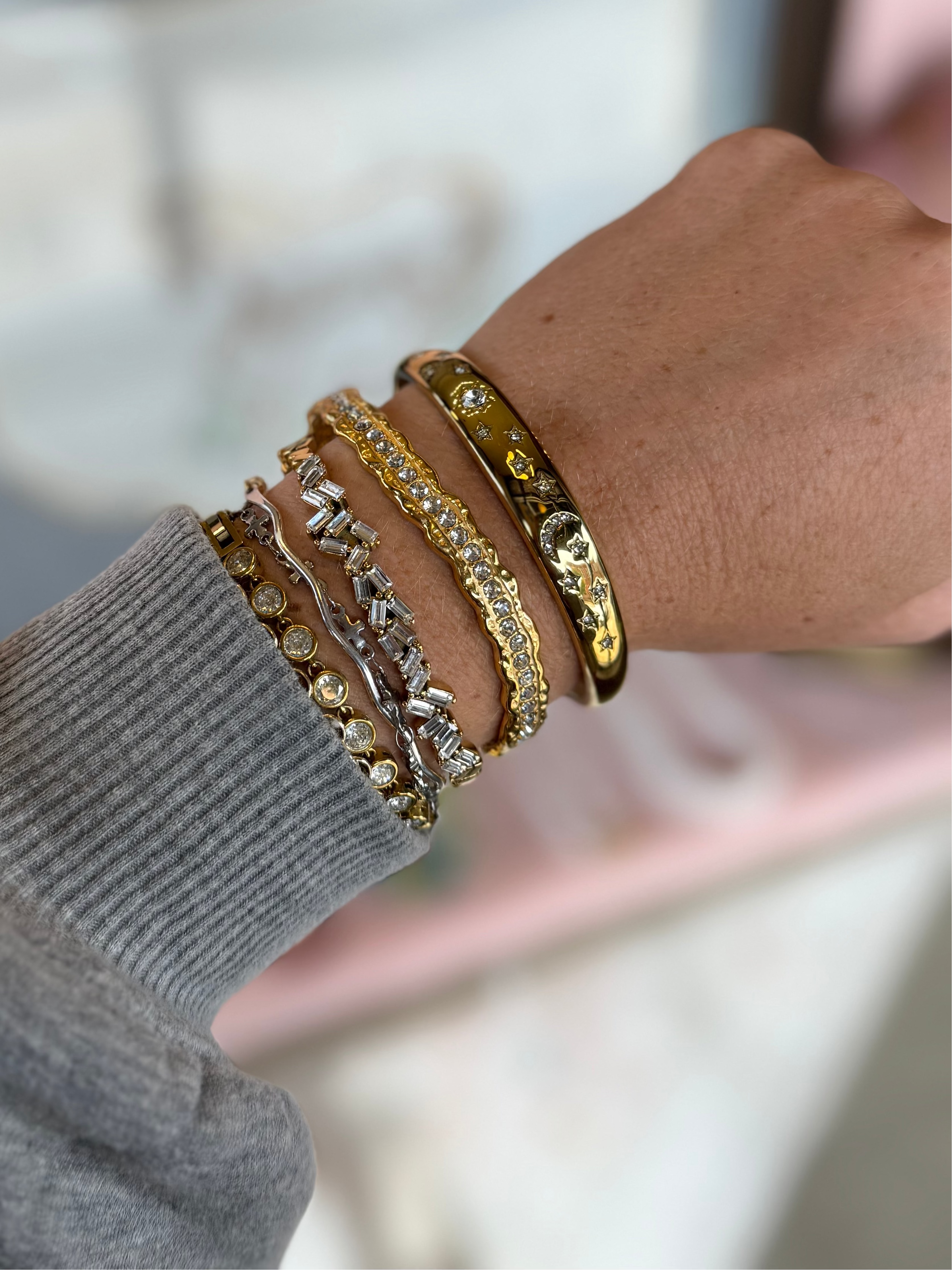 Close-up of a hand wearing multiple gold bracelets on a blurred background