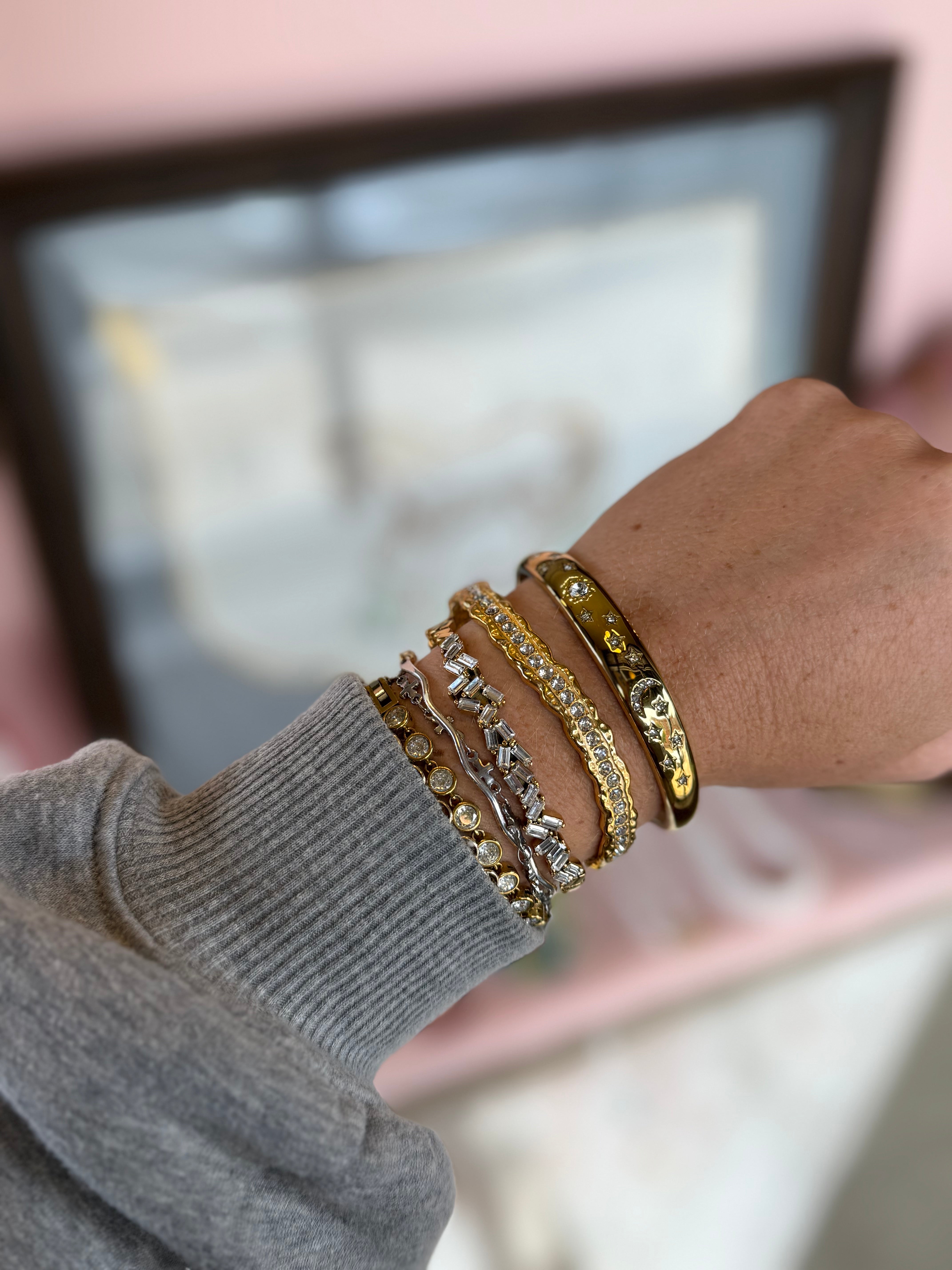 Close-up of a hand wearing multiple gold bracelets on a blurred background