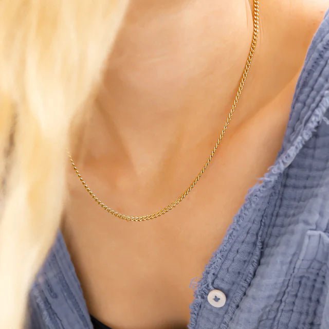 Gold curb chain necklace on a model's neck with a blue shirt.