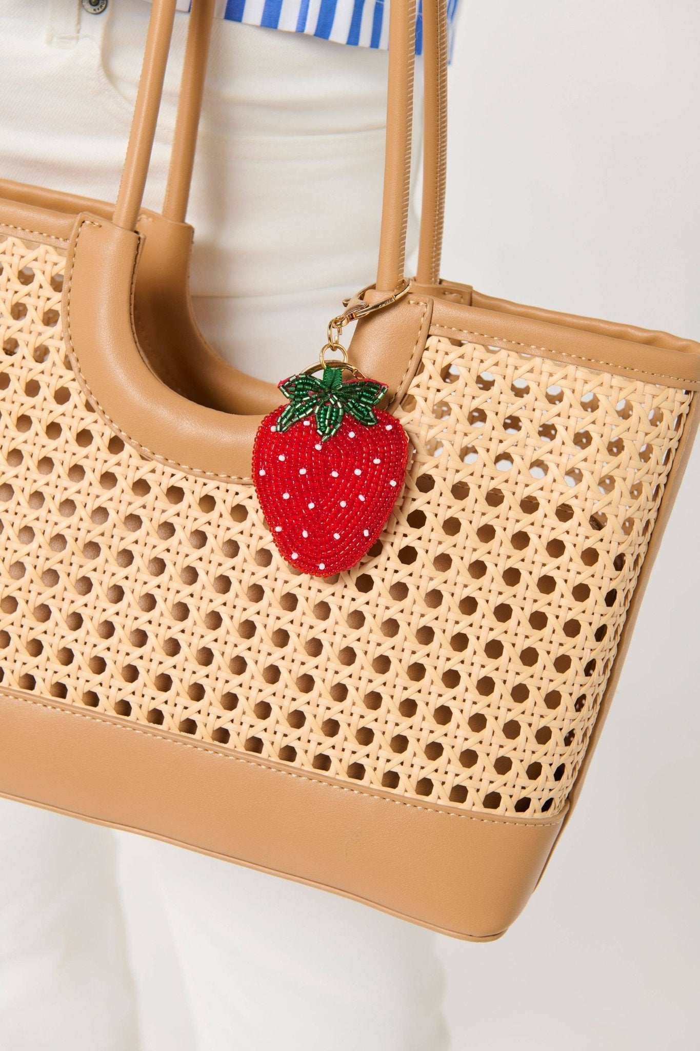Strawberry beaded bag charm/key ring by Shiraleah in red with green leaves, attached to tan woven tote