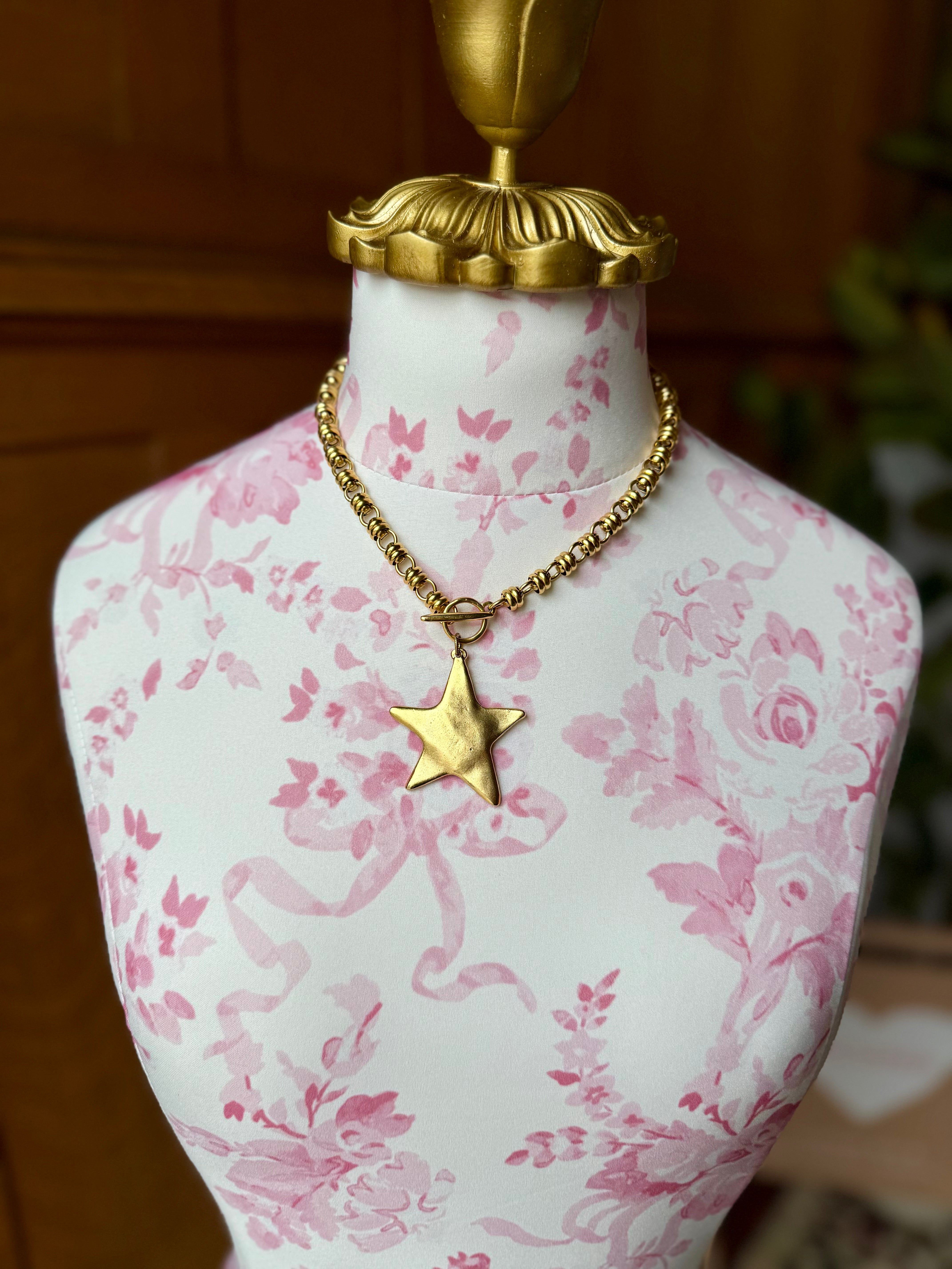 Mannequin bust with pink floral pattern wearing a gold necklace with a star pendant.