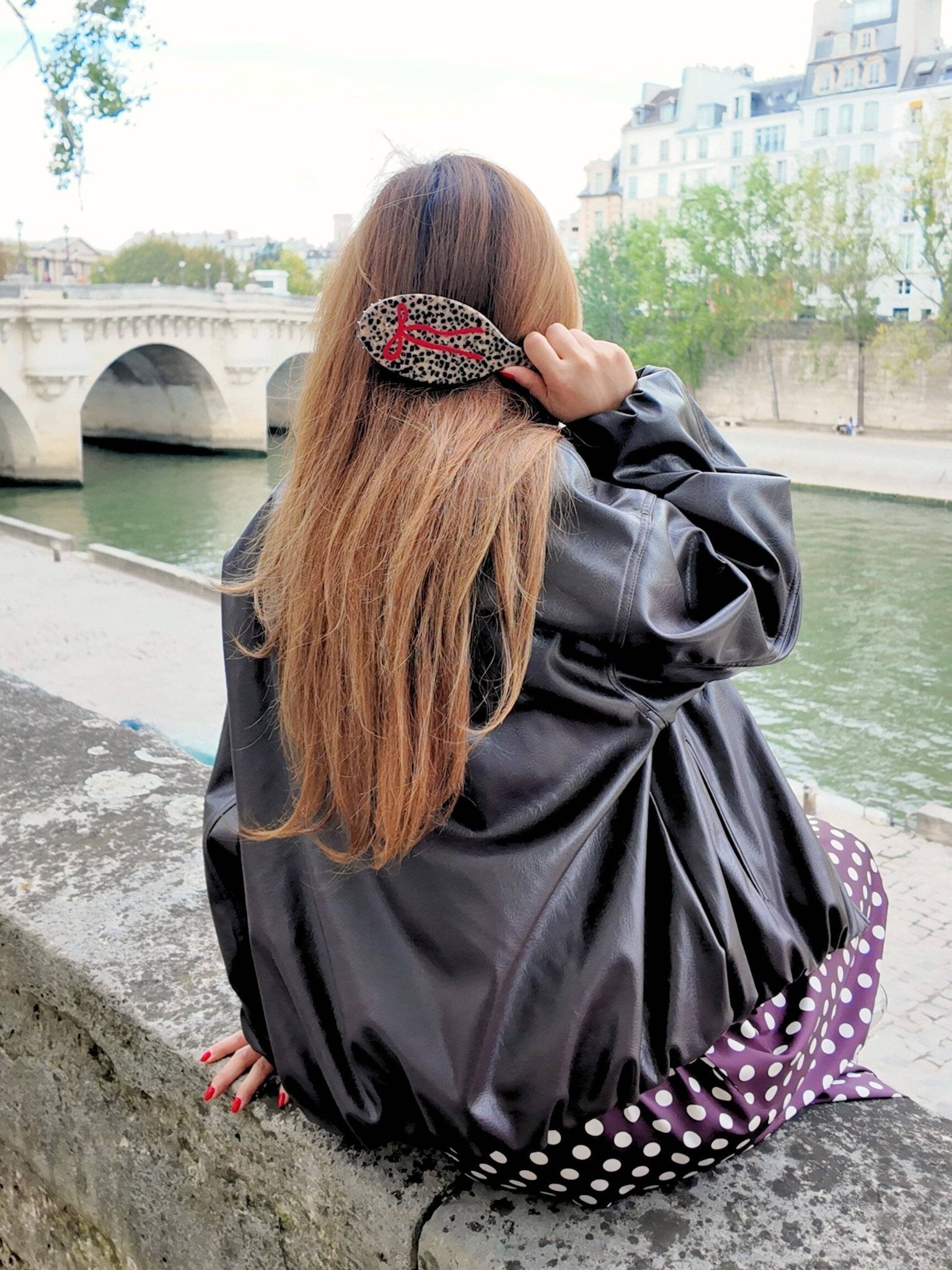Hand-painted leopard-print bow hair brush with red bow accent, worn by a woman by the river.